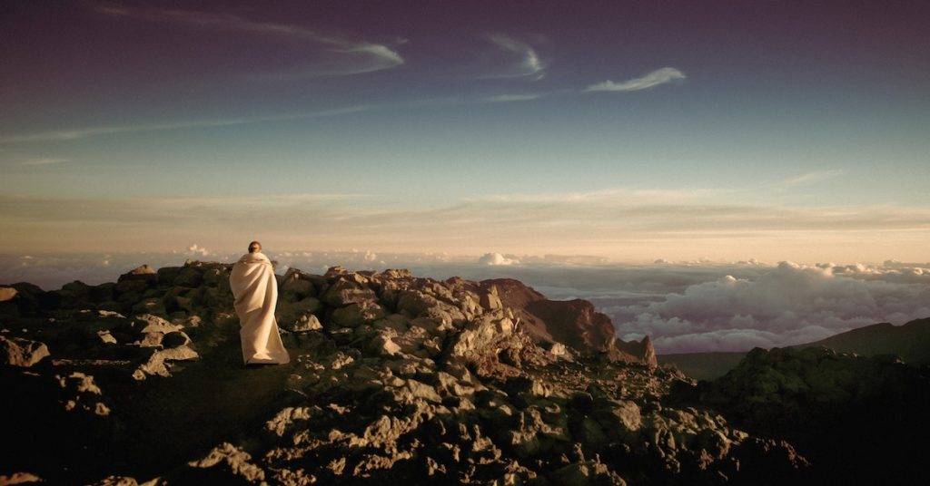 Monk in White Robe on Top of Mountains Facing Clouds